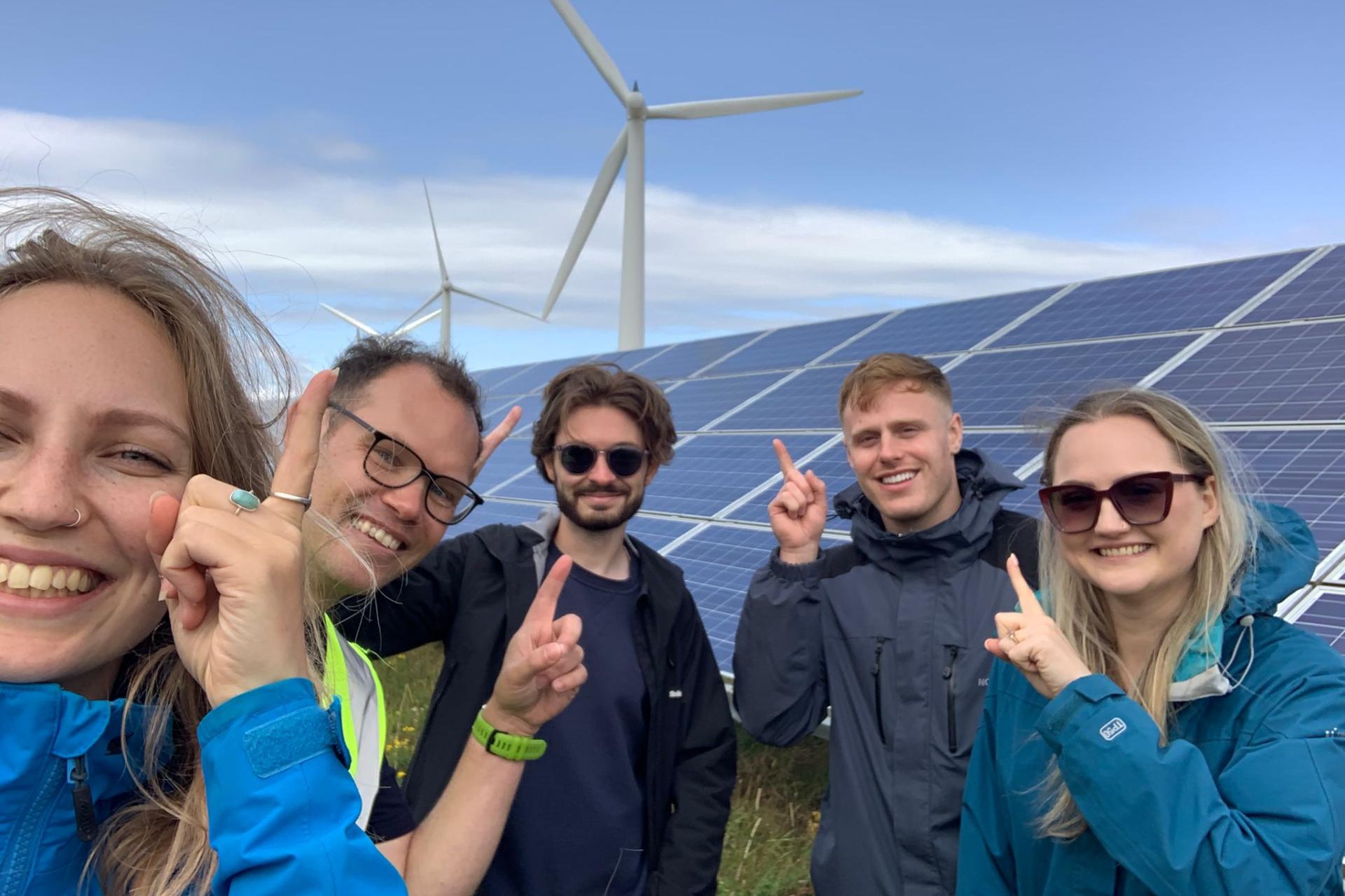 Younity team members on a renewable energy site visit, pictured infront of solar panels smiling