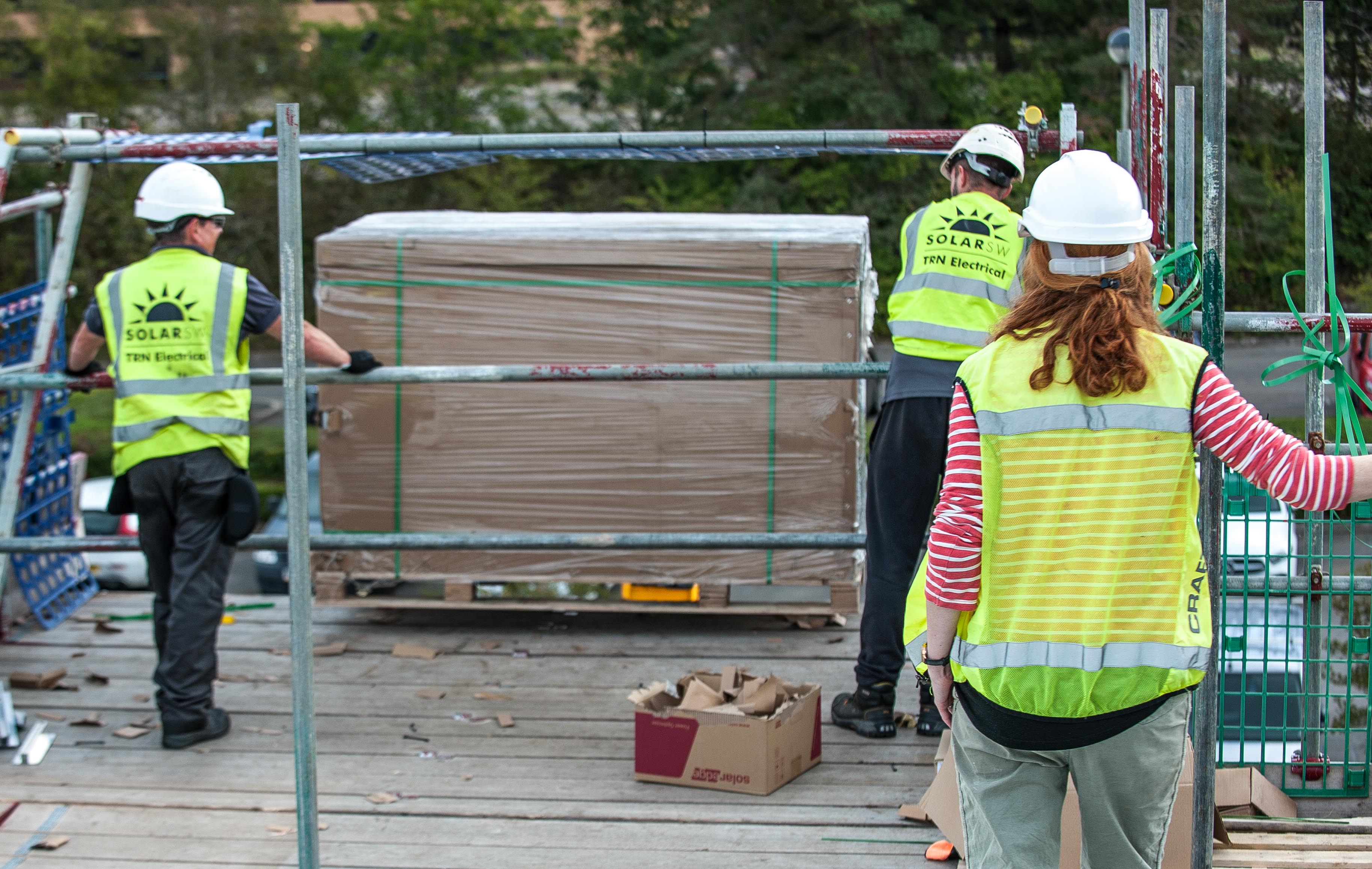 Builders transporting solar panels onto a buildings roof.