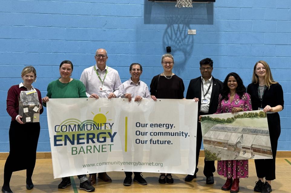 A group stood in a Sports hall behind a banner of their organisations logo.