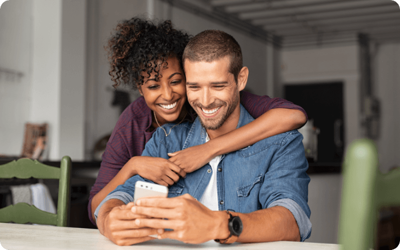 A couple hugging while using a smart phone.