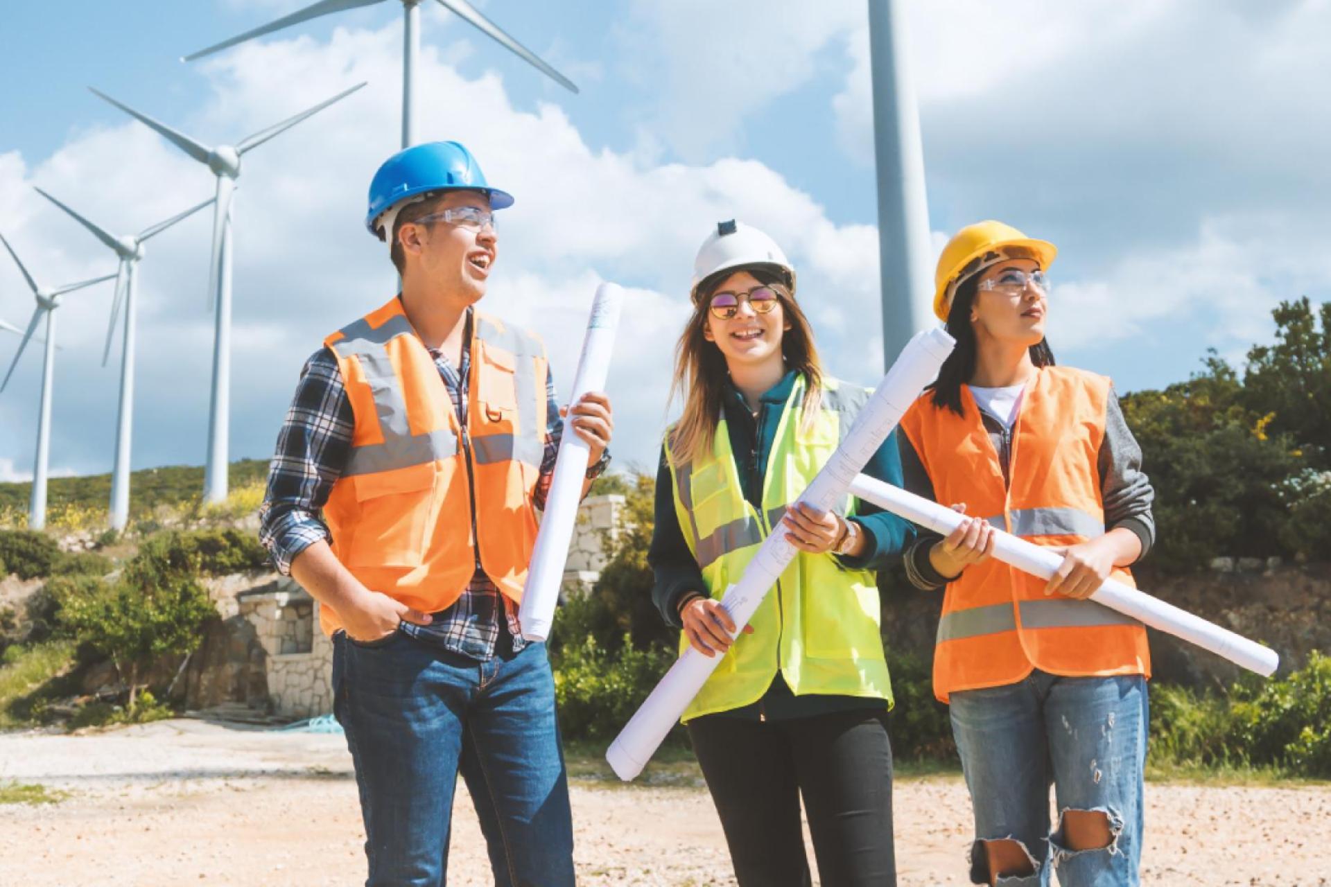 Three engineerings wearing PPE holding structural plans by a wind turbine.