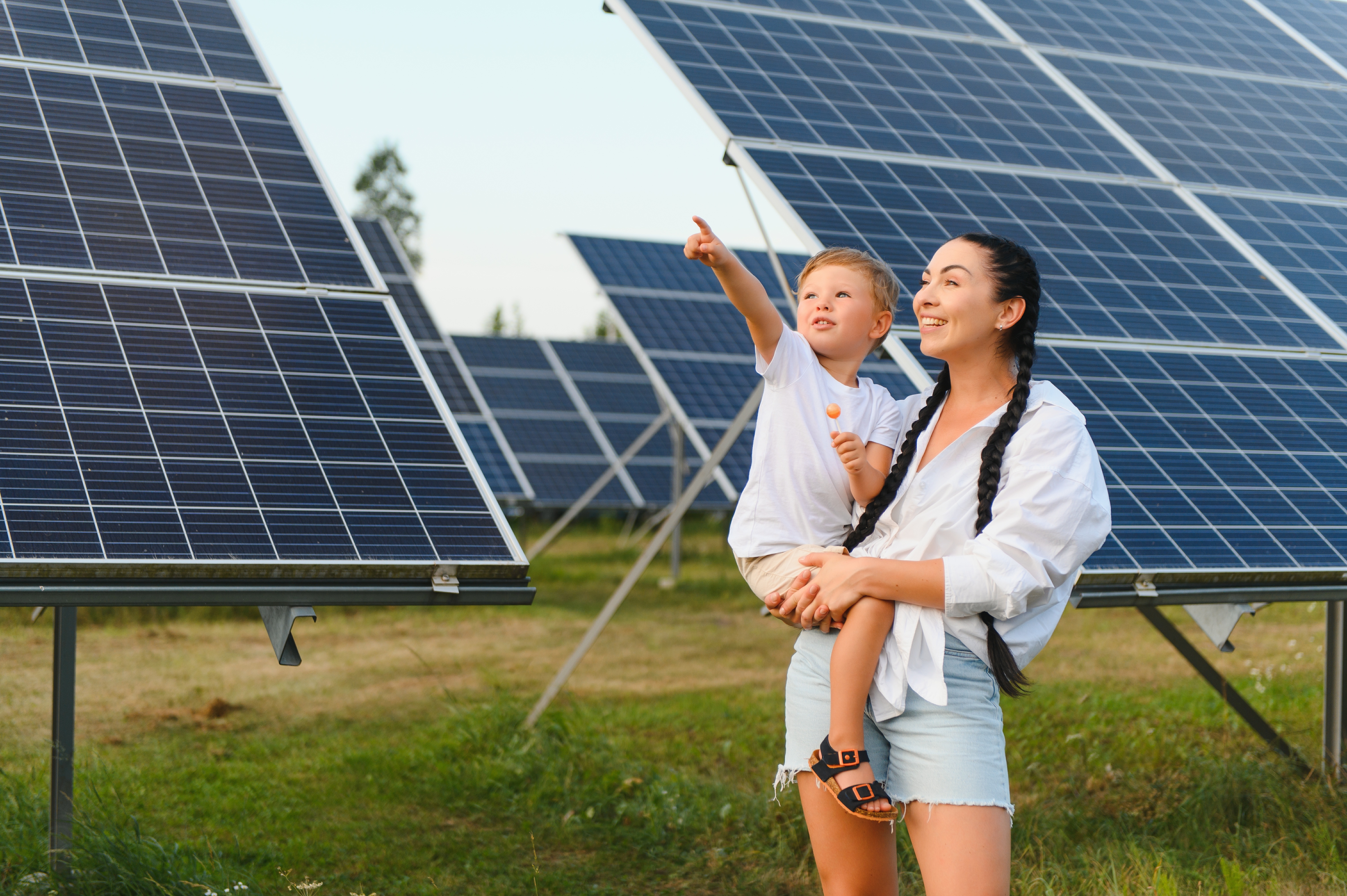 Toddler being held by their mother in front of solar panels.