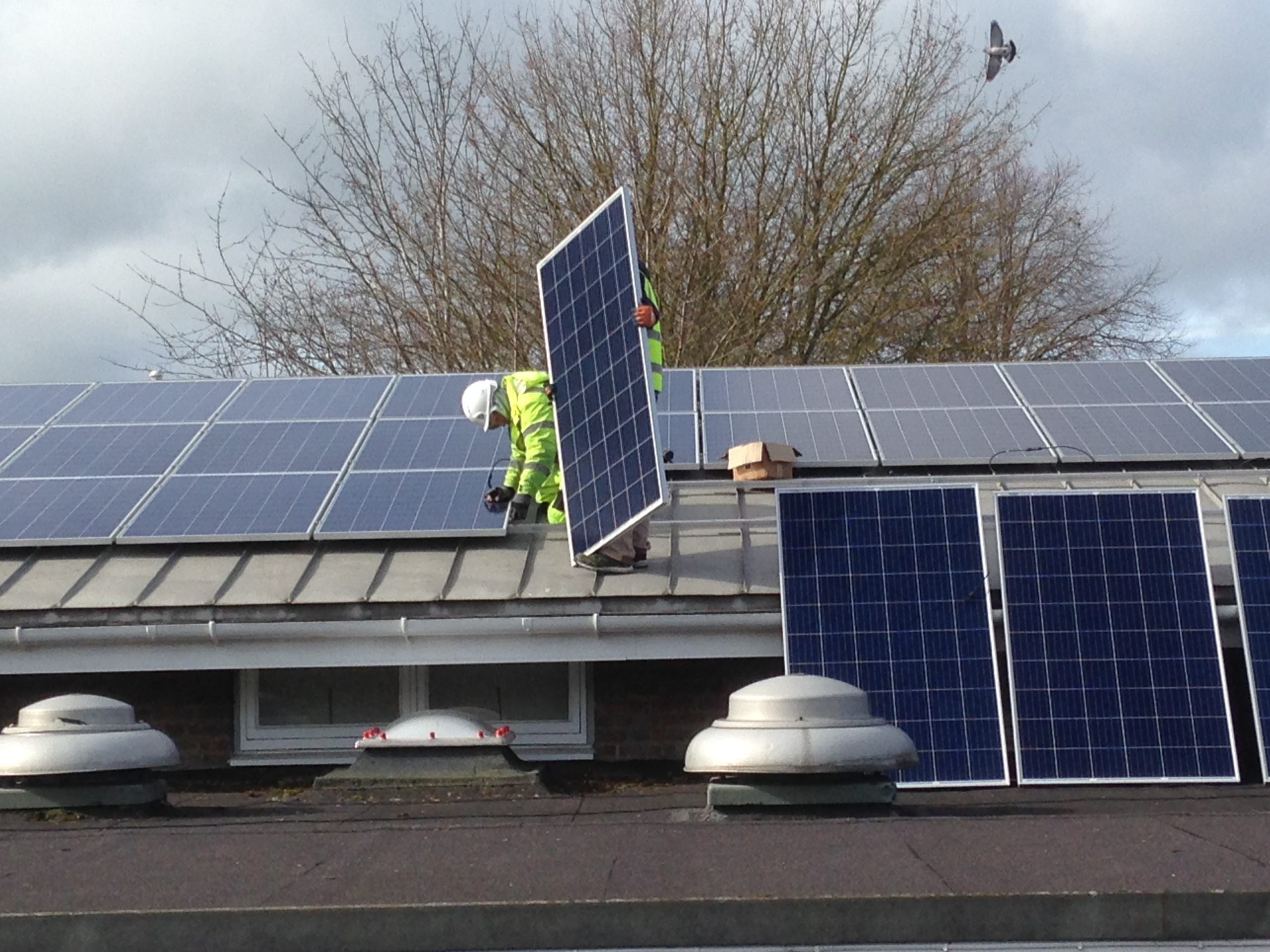 Two workers carrying solar panels across a school roof.