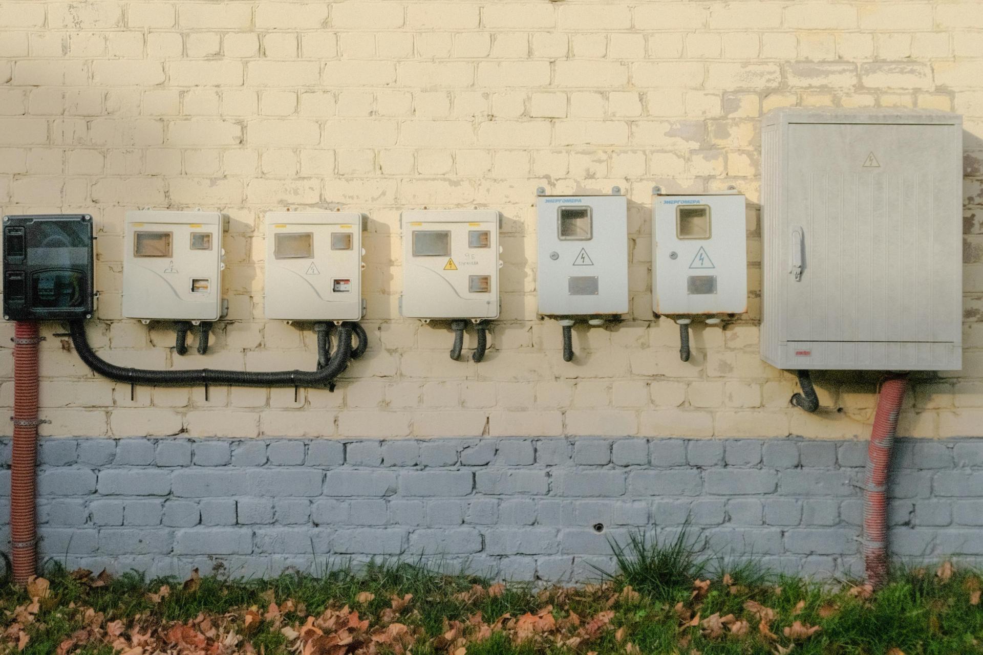 A row of 6 electricity meters fitted to a brick wall.