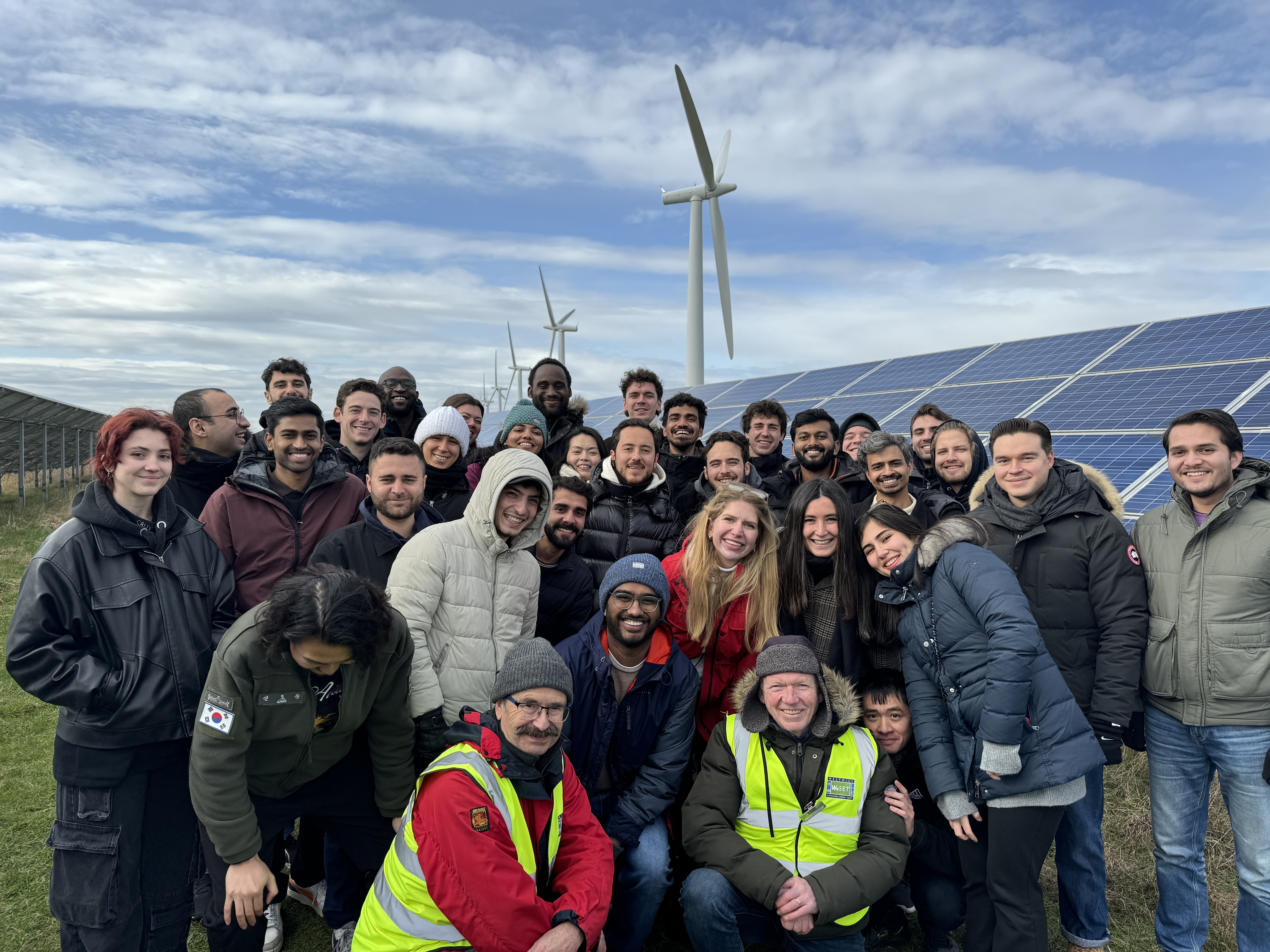 A group of students stood in a field in between rows of solar panels.