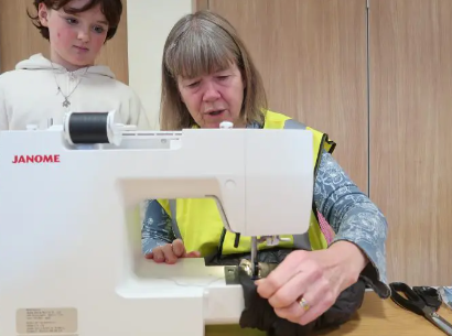 A volunteer teaching a girl how to use a sewing machine.
