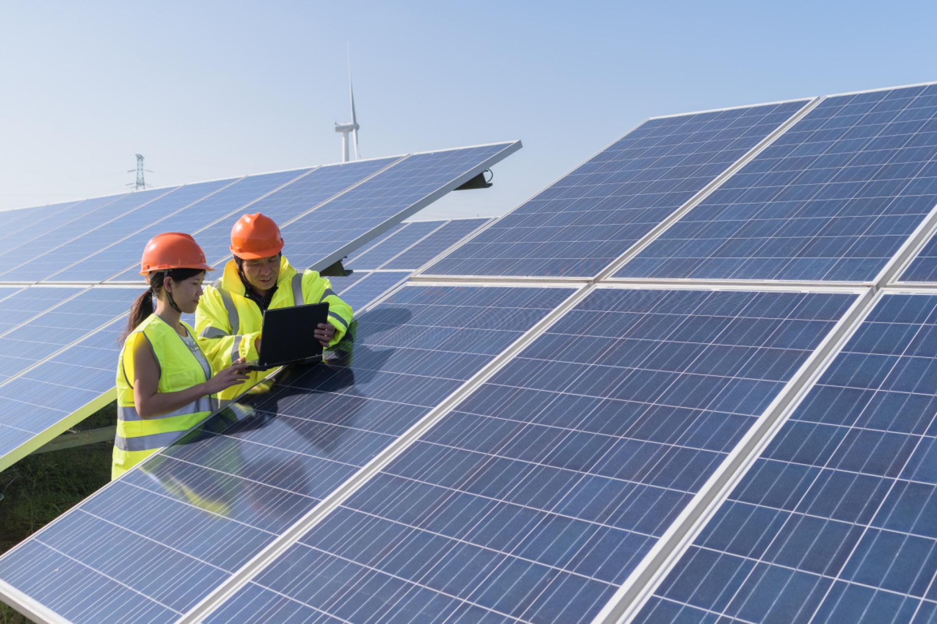 Two engineers in high-visibility jackets working by a solar panel