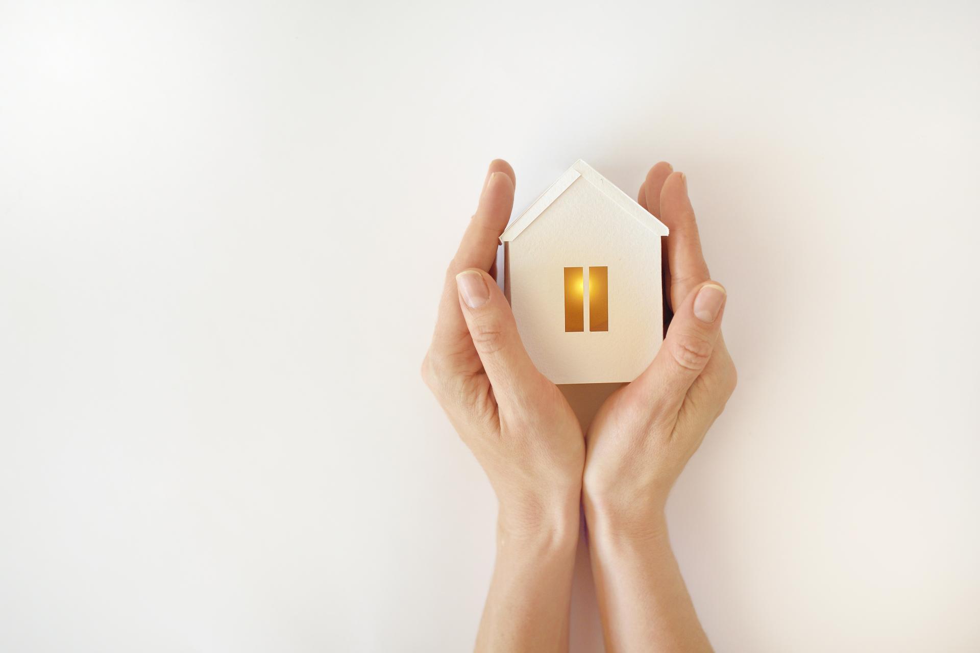 Hands gently holding a glowing house, symbolising warmth and comfort.