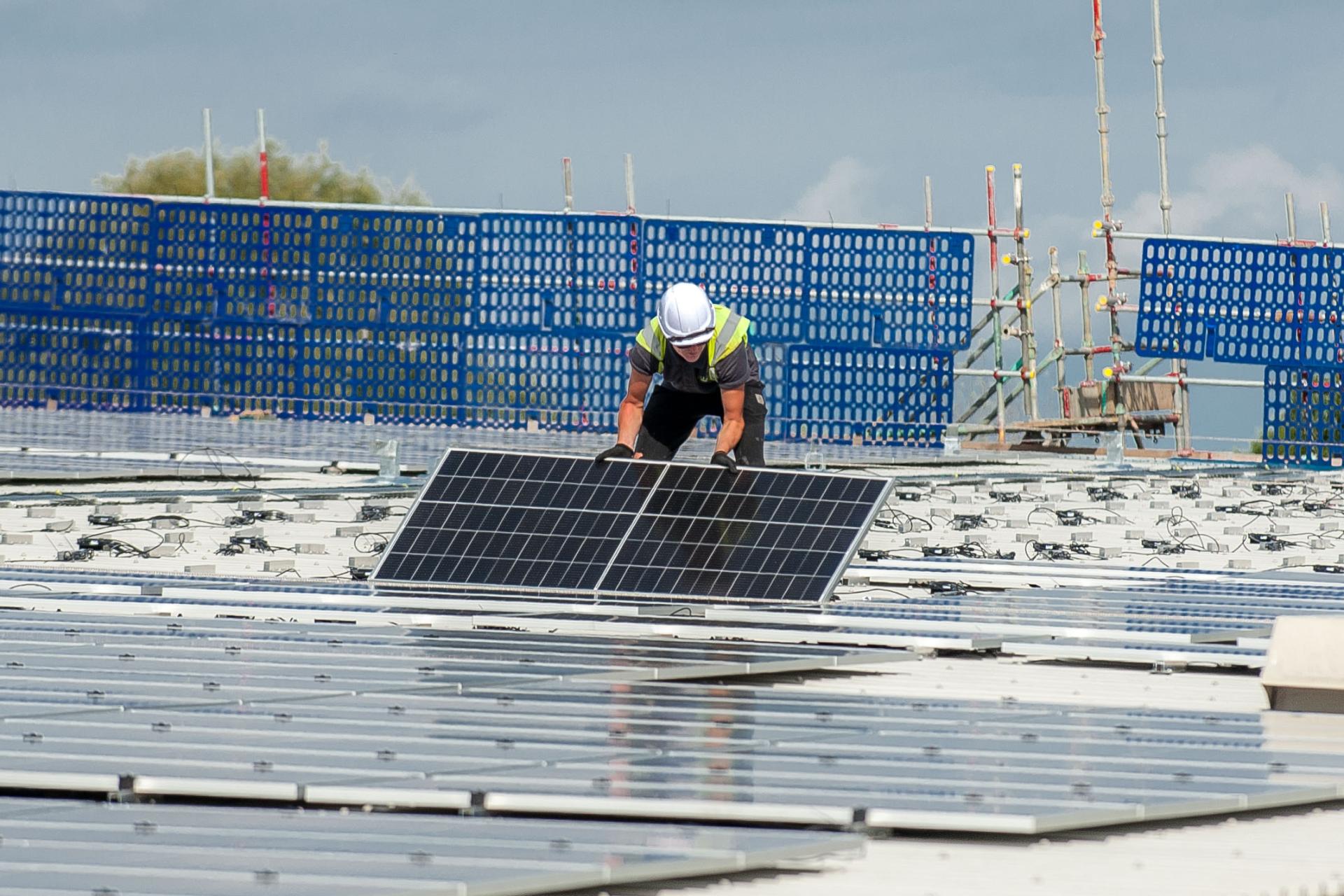 An engineer installing solar panels on a building's roof as part of a large-scale renewable energy retrofit.