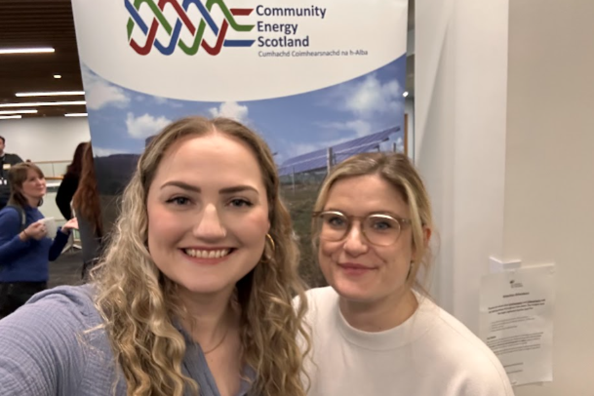 Michaela and Connie at a Community Energy Scotland conference posing in front of a banner..