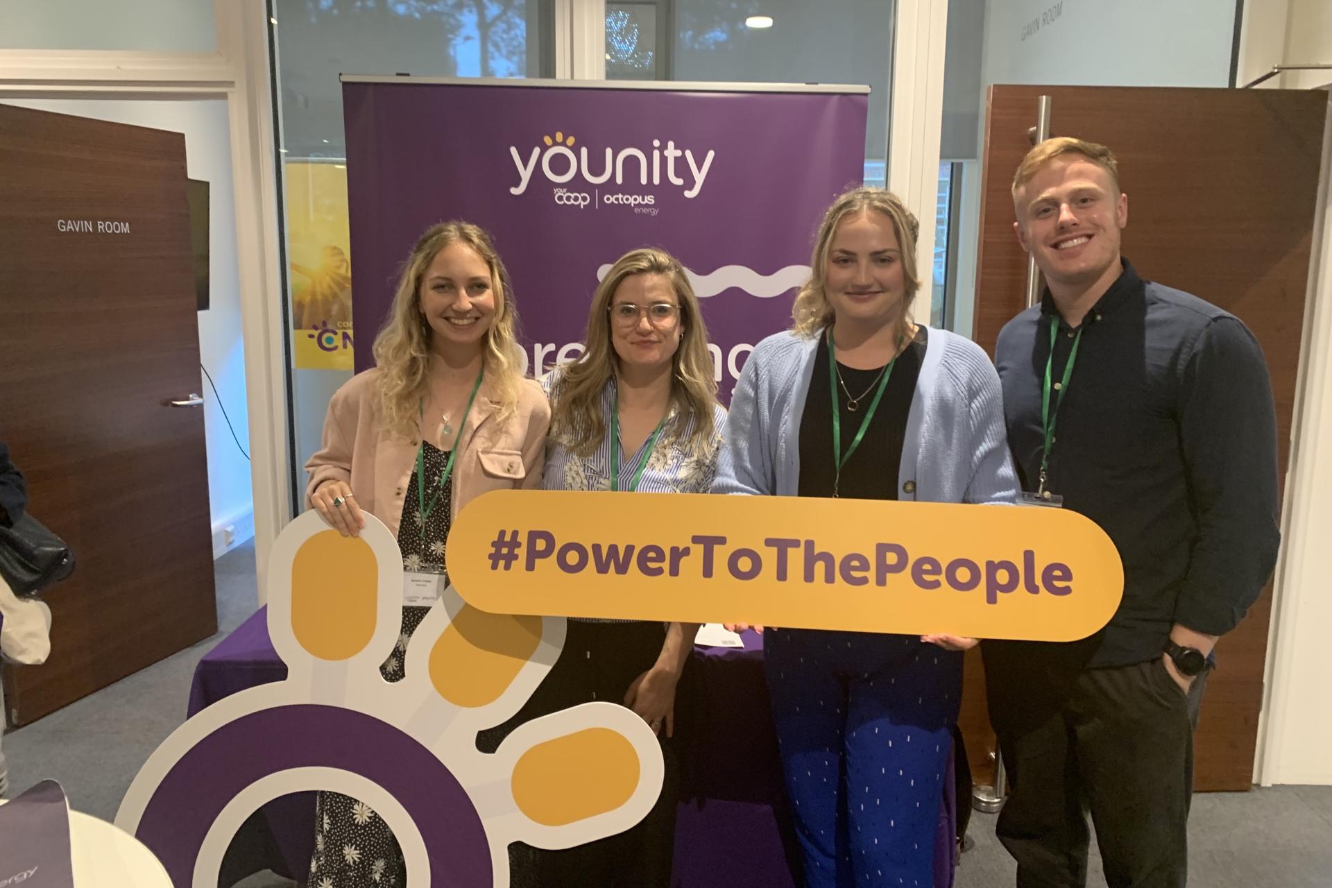 The Younity team posing with banners at a community energy event.