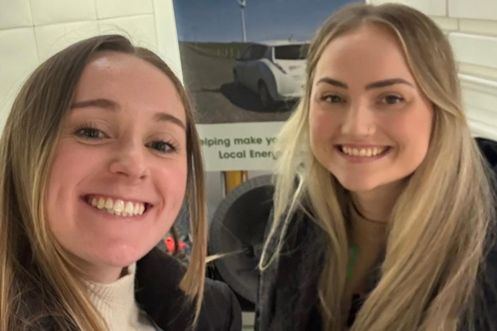 Connie & Jess at the Community Energy Scotland conference in Glasgow posing in front of a billboard