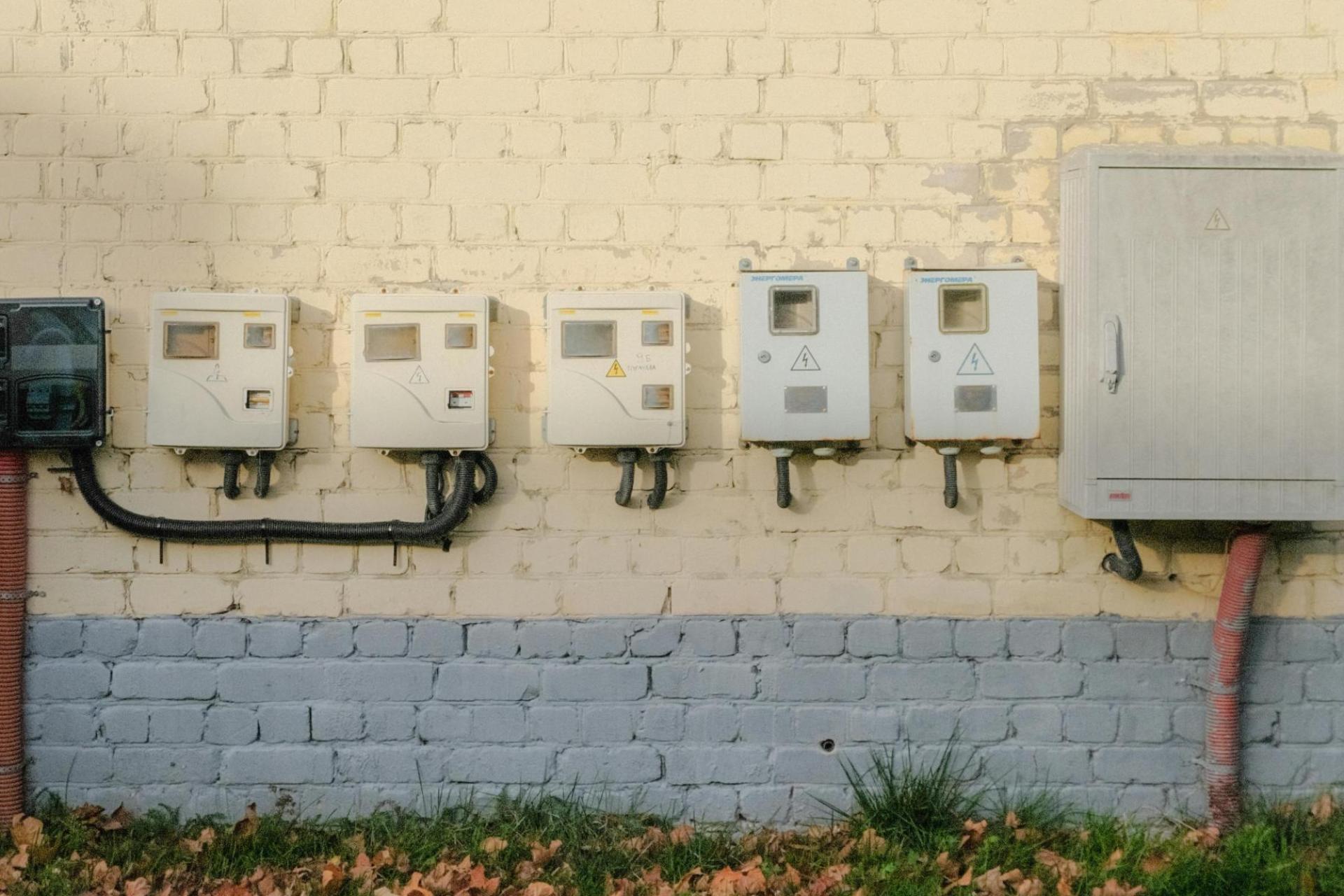 Electricity meters lined up in a row against a yellow brick wall