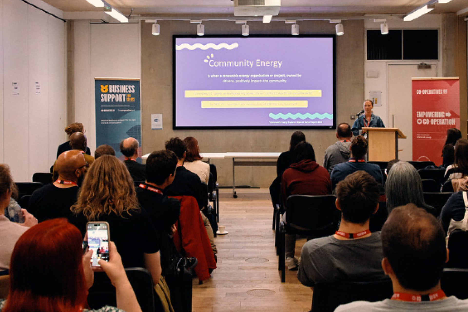 A speaker presenting to an audience in a meeting room about community energy.