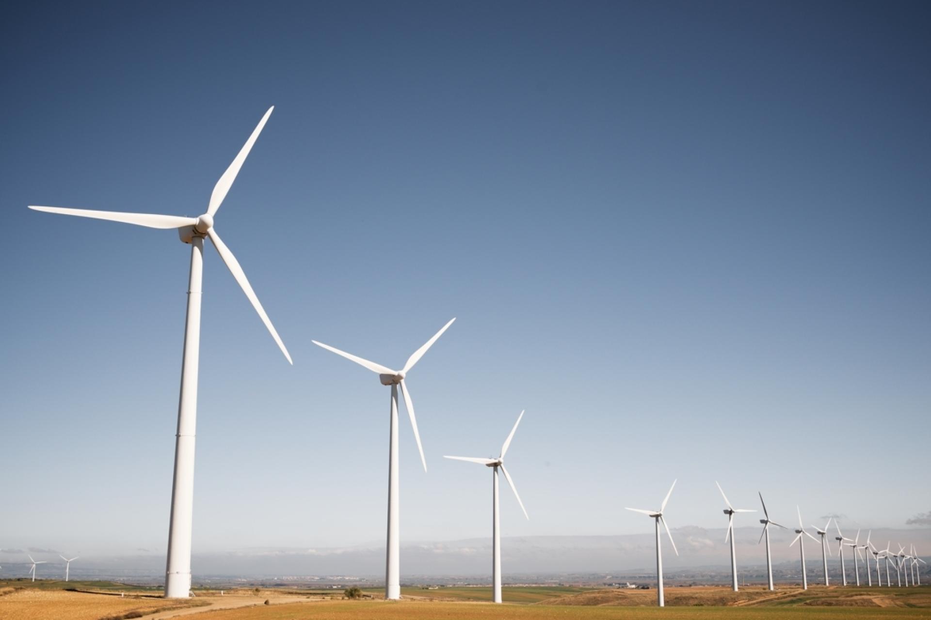 A row of 13 wind farms standing in a row in a green country field. 