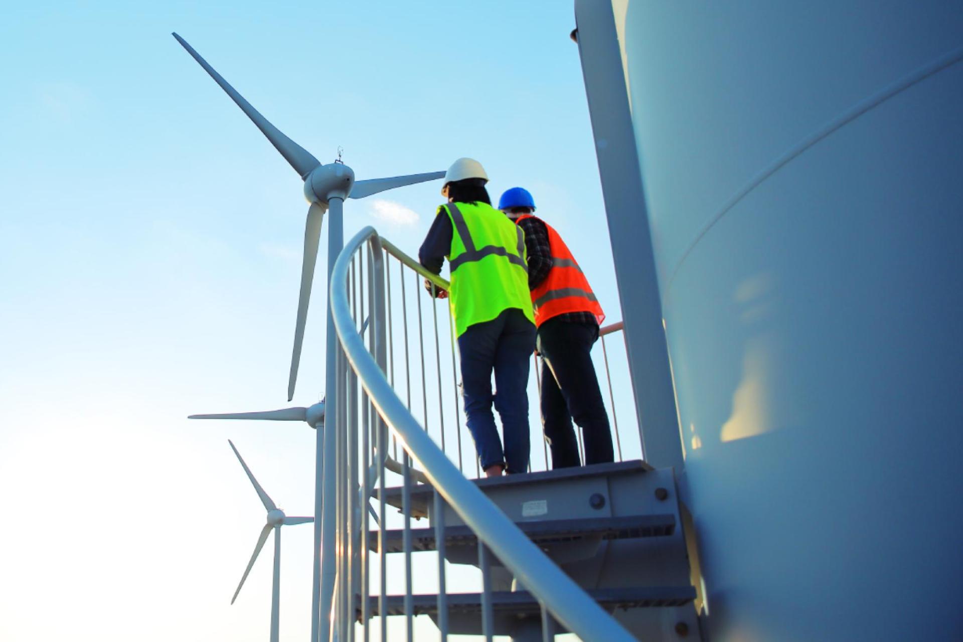 Engineers climbing the exterior stairs of a wind turbine for routine maintenance.