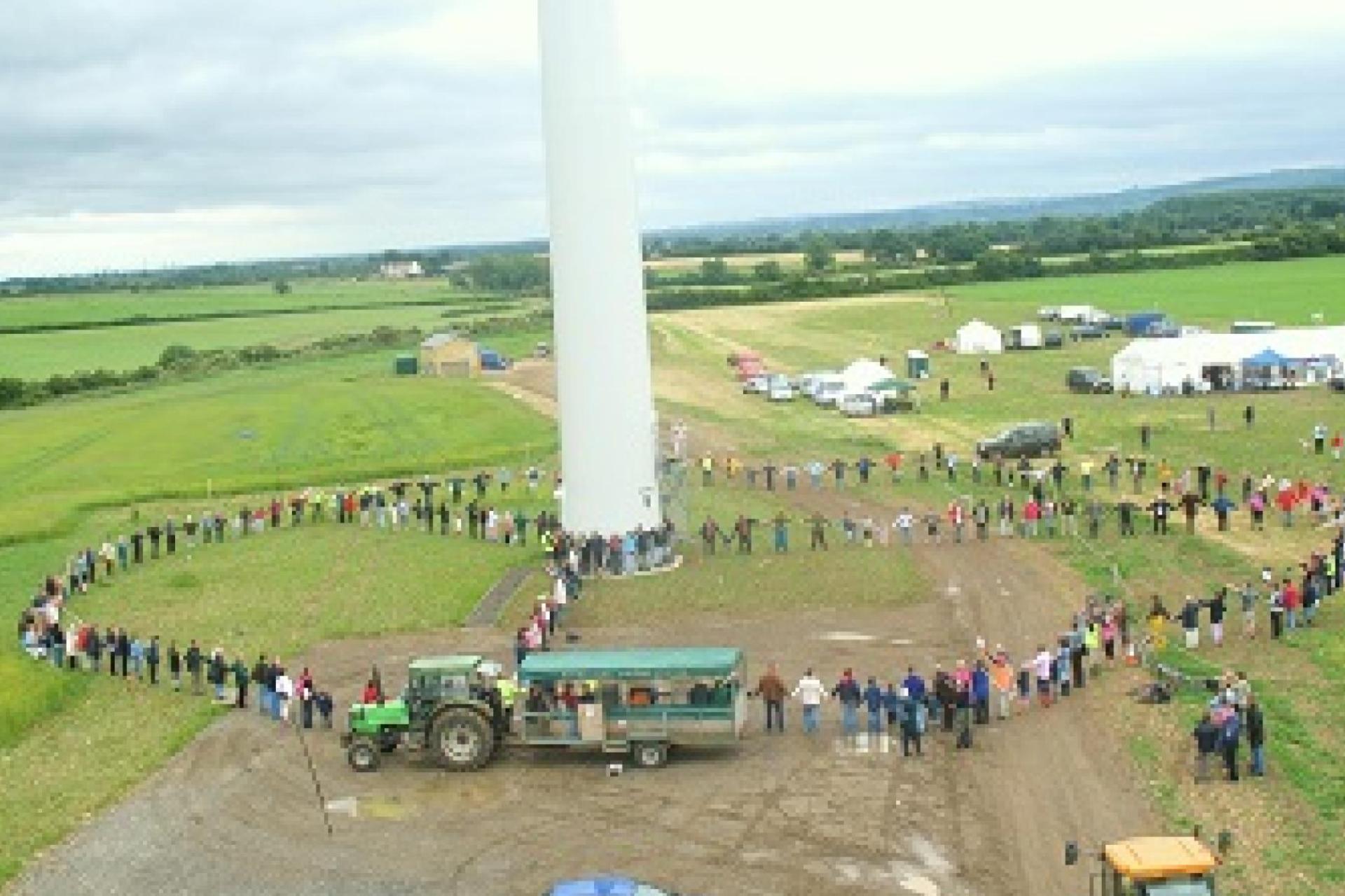 Westmill Energy members gathered by their wind turbines in a big circle holding hands.